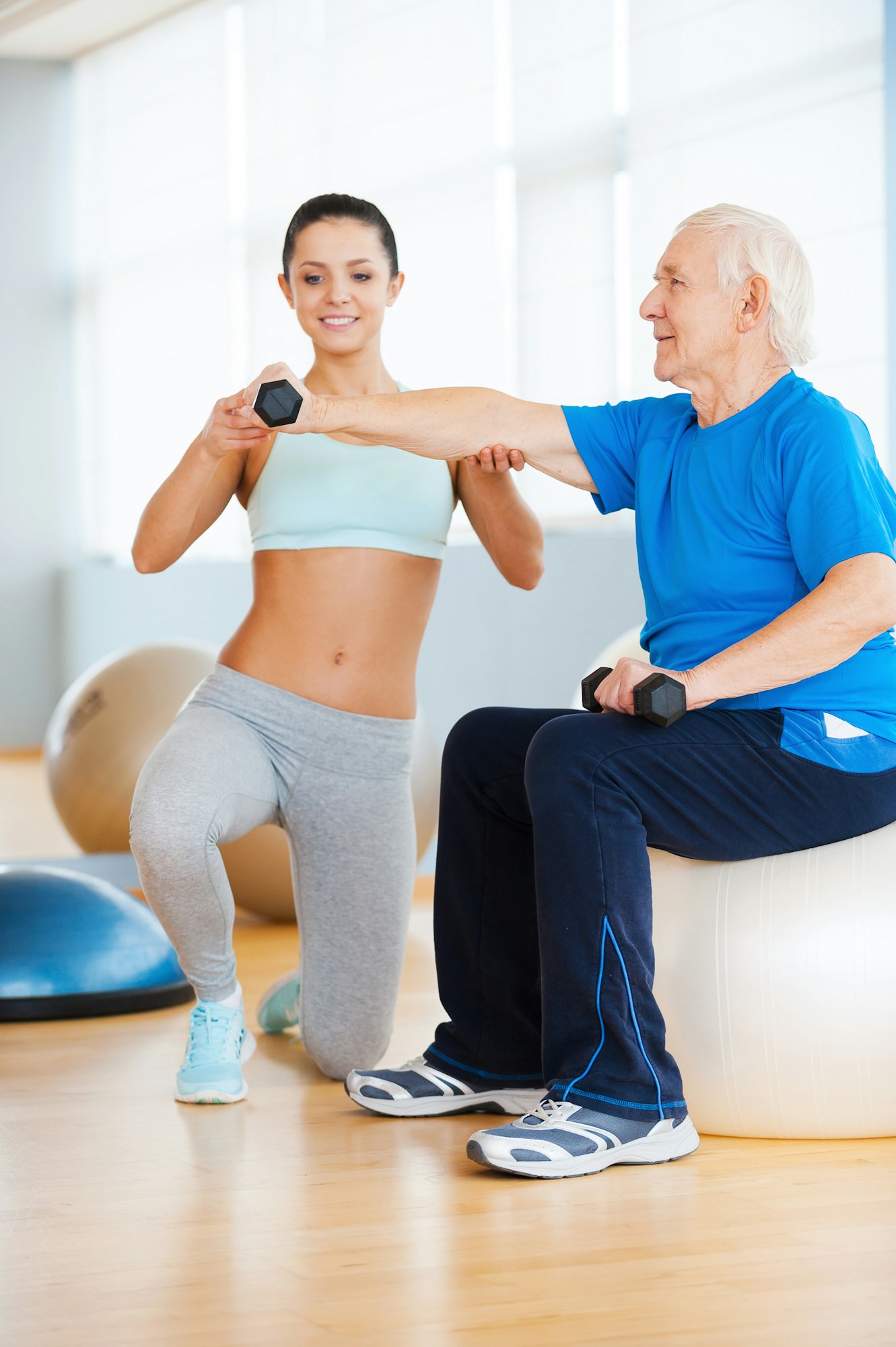 Helping to stay healthy. Confident female personal trainer helping senior man with weight exercise