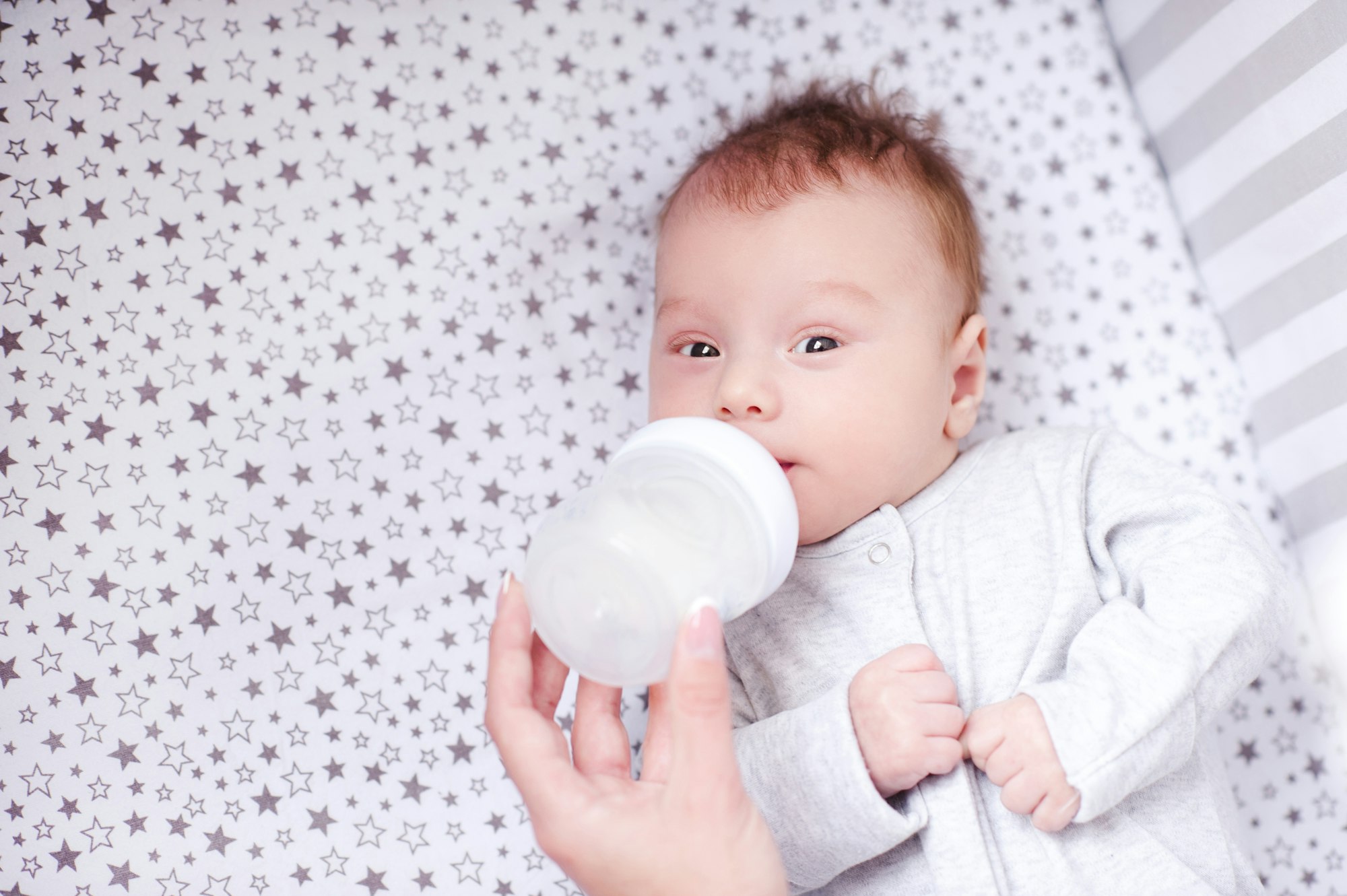 Mother feeding baby boy with milk in bed. Healthy nutrition.